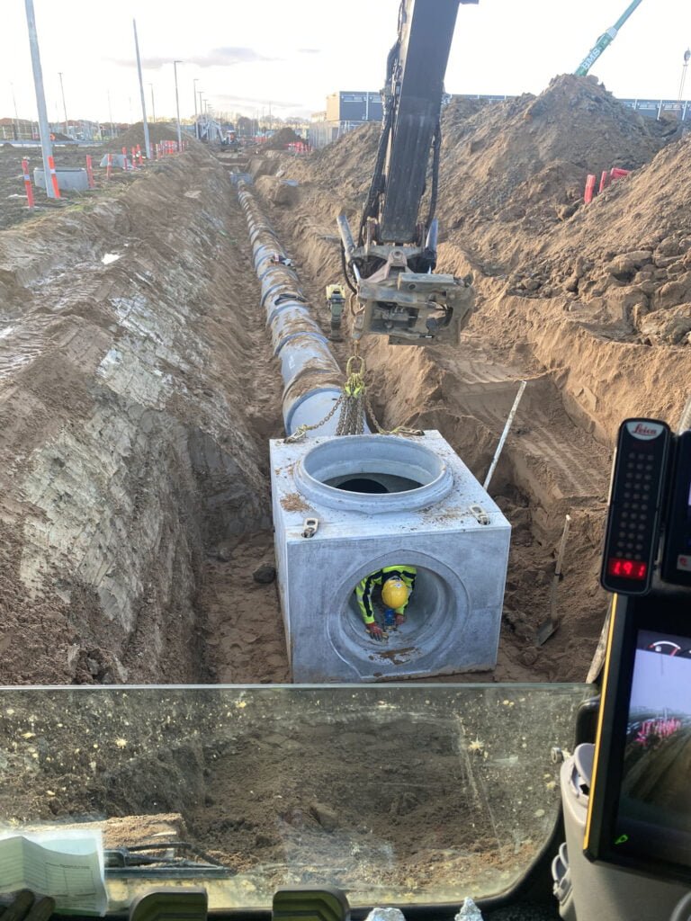 Arbejder installerer store betonrør i byggeudgravning